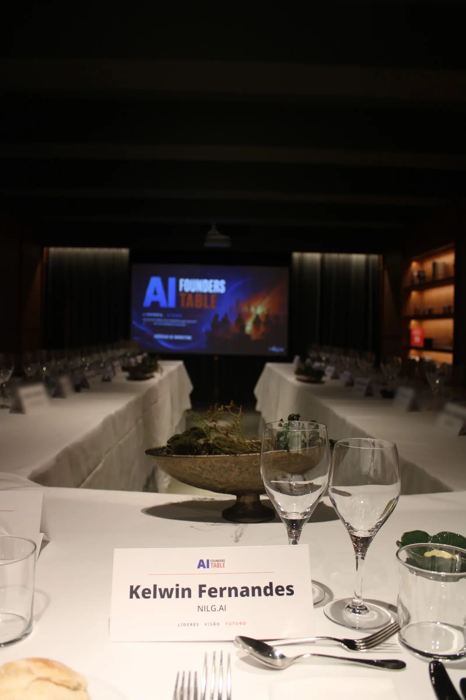 A place card at the table, with the AI Founders Table screen at the back